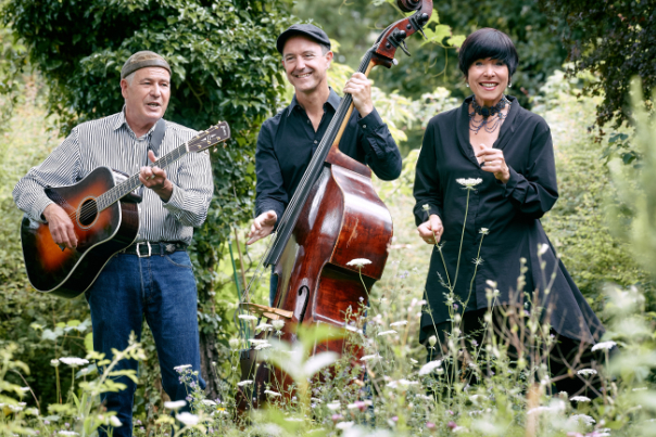 Das Foto zeigtChristof Altmamm, Florian Dohrmann und Vladislava Altmann auf einer Wiese mit ihren Instrumenten